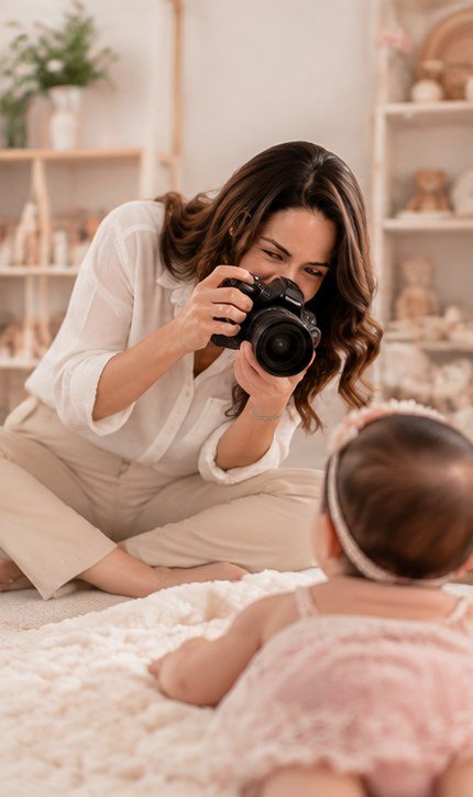 Adriana fotografando um bebê deitado no tapete do estúdio